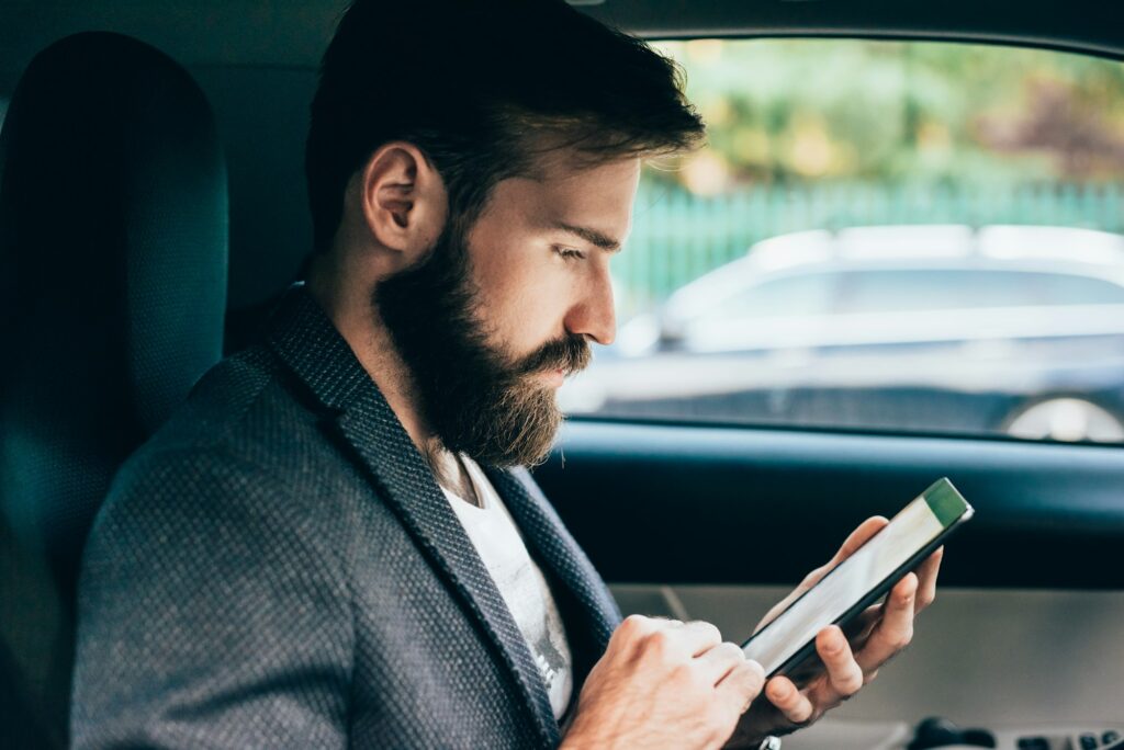 young bearded man using smartphone sitting car